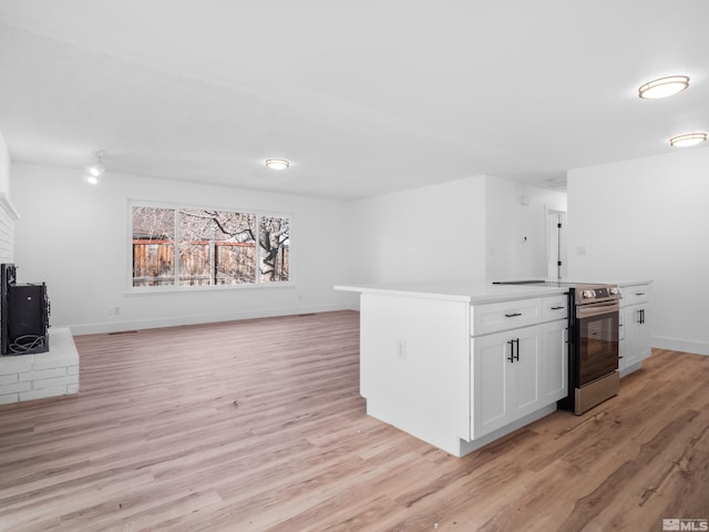 kitchen with a fireplace, light wood-type flooring, stainless steel range with electric stovetop, and white cabinetry