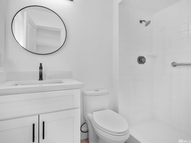 bathroom with toilet, a tile shower, and vanity