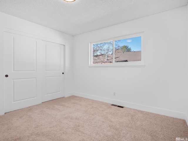 unfurnished bedroom with a closet, light carpet, and a textured ceiling