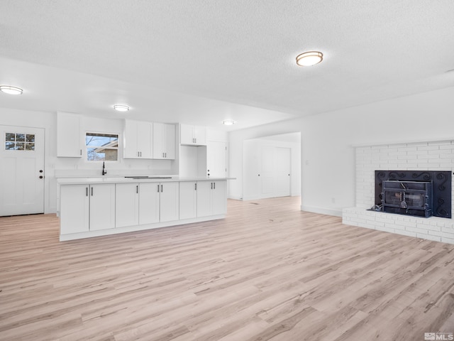 unfurnished living room featuring light hardwood / wood-style floors, sink, a textured ceiling, and a wood stove