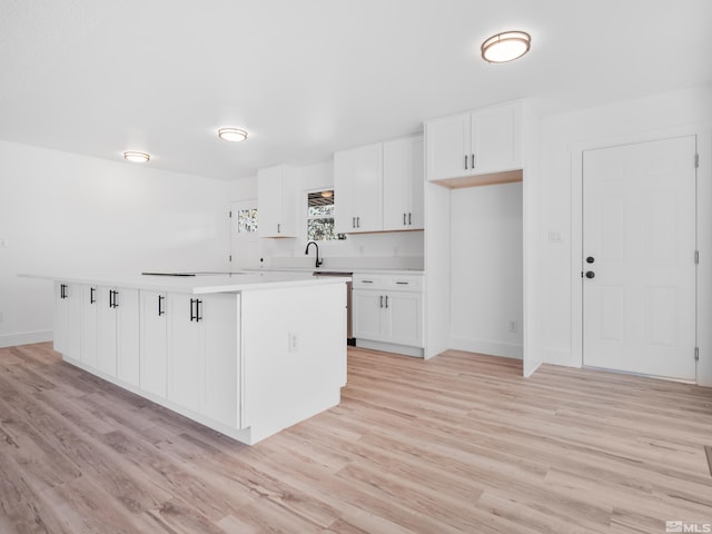 kitchen with sink, white cabinetry, light wood-type flooring, and a kitchen island