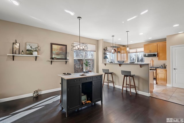 kitchen featuring hanging light fixtures, a center island, stainless steel appliances, light brown cabinetry, and a breakfast bar