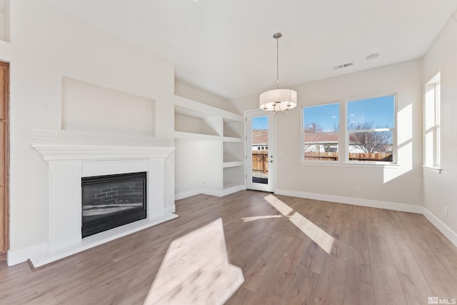 unfurnished living room featuring built in shelves, an inviting chandelier, and light wood-type flooring