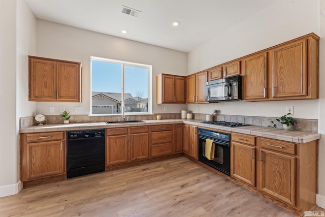 kitchen featuring black appliances, light hardwood / wood-style flooring, sink, and tile counters