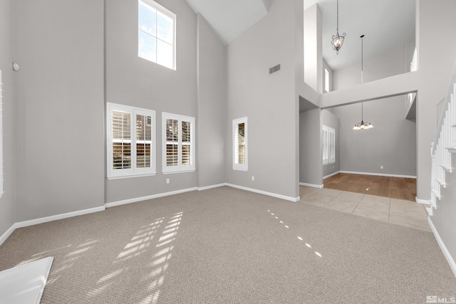 unfurnished living room featuring a towering ceiling, light carpet, and a notable chandelier