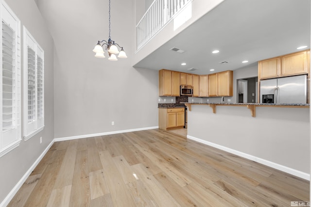 kitchen featuring stainless steel appliances, decorative light fixtures, a kitchen bar, kitchen peninsula, and a notable chandelier