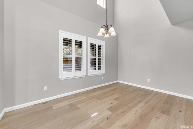 unfurnished dining area with a towering ceiling, light wood-type flooring, and a notable chandelier