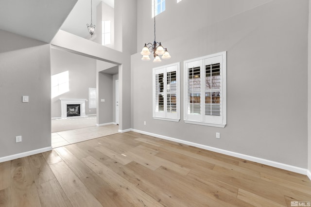 unfurnished dining area featuring a notable chandelier, a wealth of natural light, a towering ceiling, and wood-type flooring