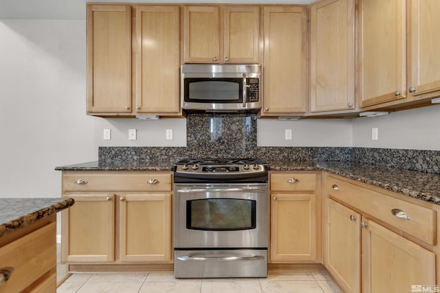 kitchen with stainless steel appliances, light brown cabinets, light tile patterned floors, and dark stone counters