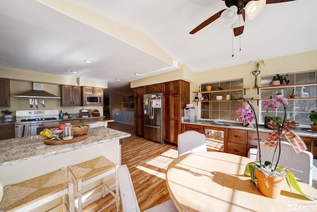 kitchen featuring light stone counters, wall chimney exhaust hood, stainless steel appliances, lofted ceiling, and light wood-type flooring