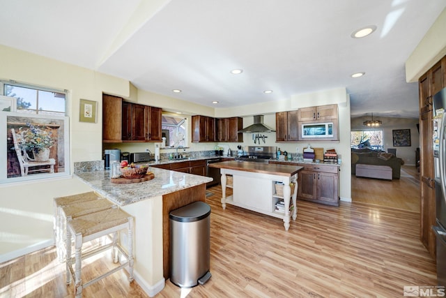 kitchen with sink, light hardwood / wood-style floors, stove, wall chimney range hood, and a breakfast bar