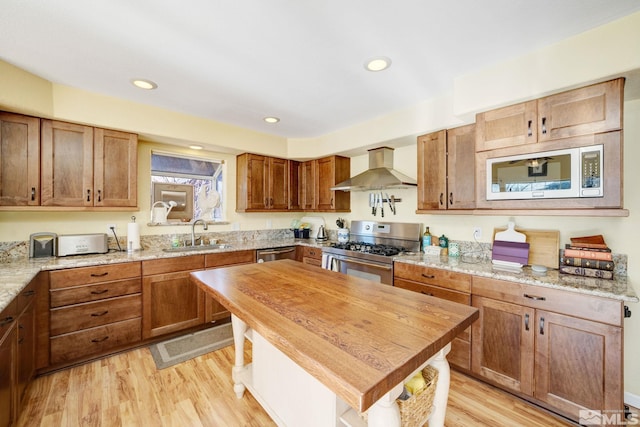 kitchen featuring stainless steel appliances, light stone countertops, sink, light hardwood / wood-style flooring, and wall chimney range hood