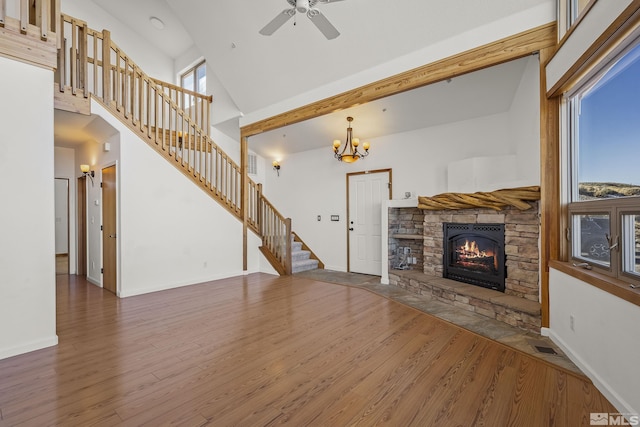 unfurnished living room with ceiling fan with notable chandelier, hardwood / wood-style flooring, high vaulted ceiling, and a fireplace