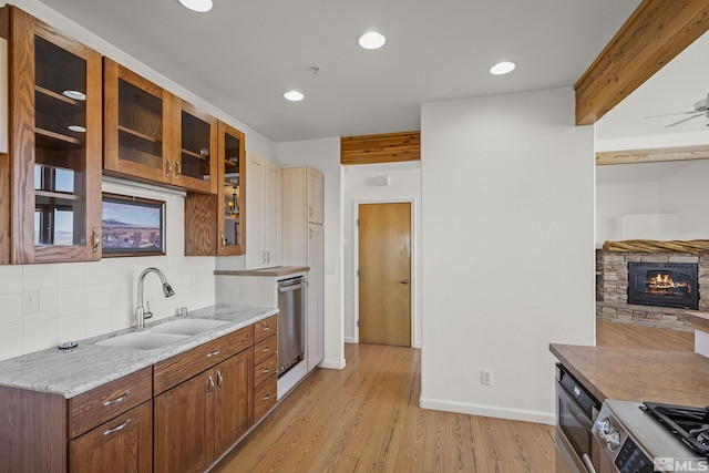 kitchen with sink, stainless steel appliances, light hardwood / wood-style floors, beamed ceiling, and a stone fireplace