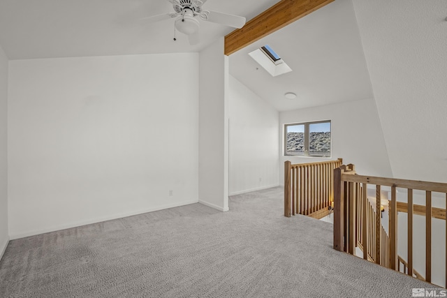 spare room with ceiling fan, vaulted ceiling with skylight, and light colored carpet