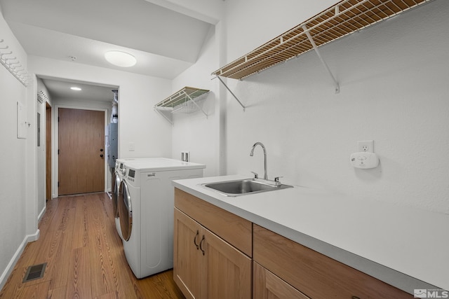 laundry room featuring sink, washer and dryer, and light hardwood / wood-style flooring