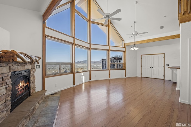 unfurnished living room featuring a stone fireplace, wood-type flooring, ceiling fan, high vaulted ceiling, and a mountain view