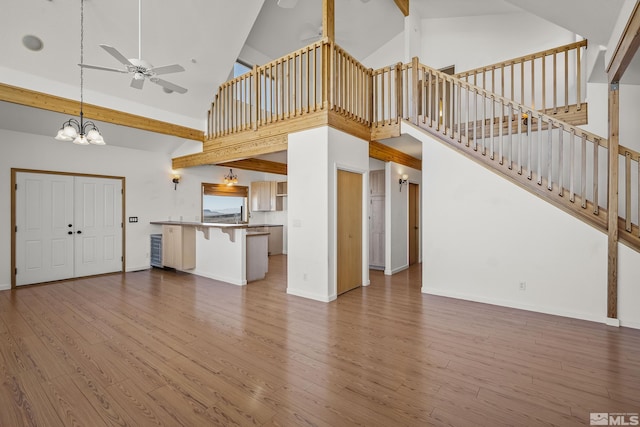 unfurnished living room with ceiling fan with notable chandelier, high vaulted ceiling, and hardwood / wood-style floors