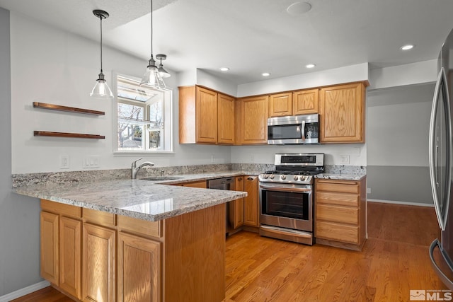 kitchen with kitchen peninsula, appliances with stainless steel finishes, decorative light fixtures, light stone countertops, and sink