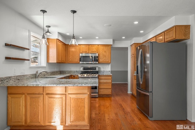 kitchen with hardwood / wood-style floors, kitchen peninsula, stainless steel appliances, decorative light fixtures, and sink