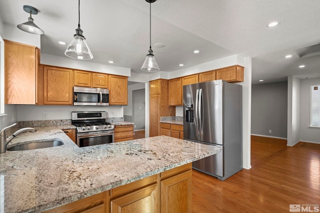 kitchen featuring kitchen peninsula, appliances with stainless steel finishes, light stone countertops, pendant lighting, and sink