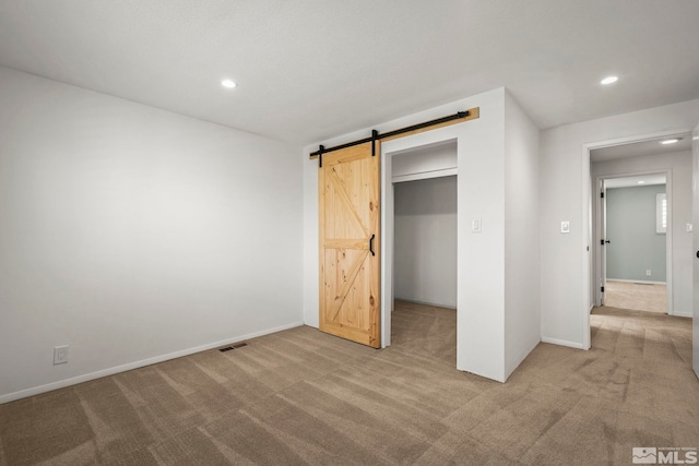 unfurnished bedroom with a closet, light carpet, and a barn door