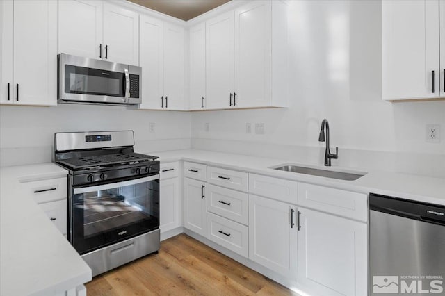 kitchen featuring appliances with stainless steel finishes, light hardwood / wood-style floors, white cabinets, and sink