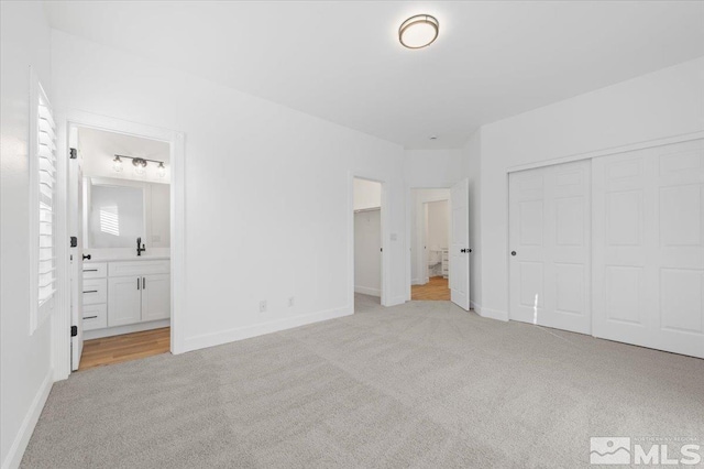 unfurnished bedroom with sink, light colored carpet, a closet, and connected bathroom