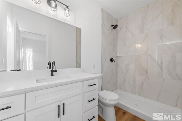 bathroom with toilet, hardwood / wood-style flooring, tiled shower, and vanity