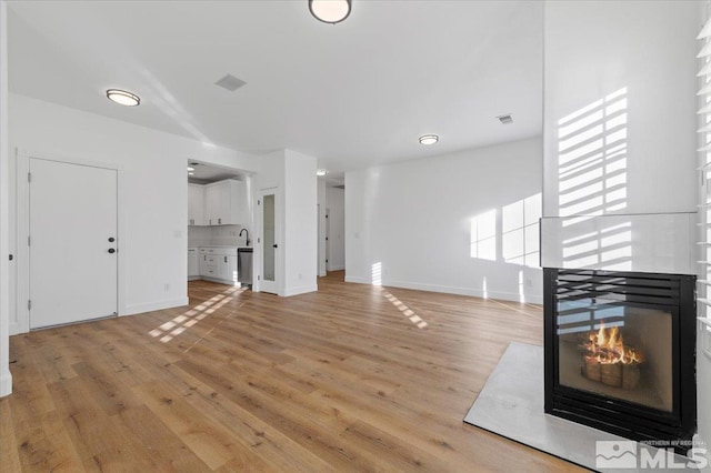 unfurnished living room with light hardwood / wood-style flooring and a multi sided fireplace