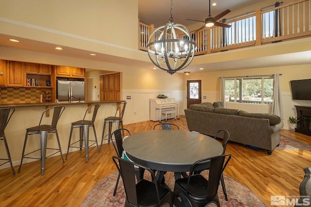 dining area with a towering ceiling, light hardwood / wood-style floors, and ceiling fan with notable chandelier