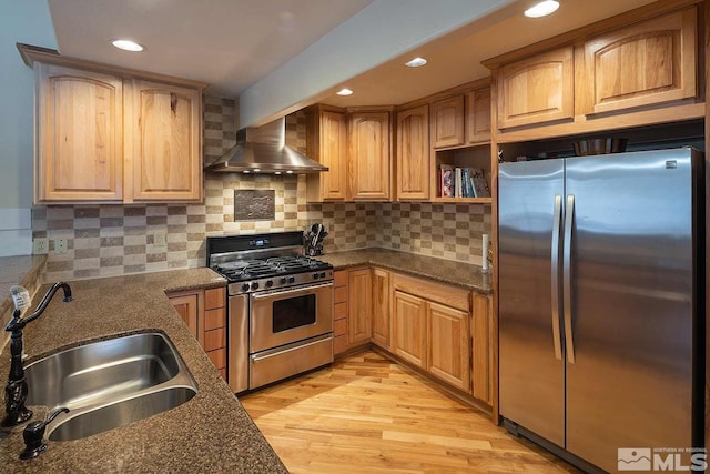 kitchen with stainless steel appliances, sink, decorative backsplash, dark stone counters, and wall chimney range hood