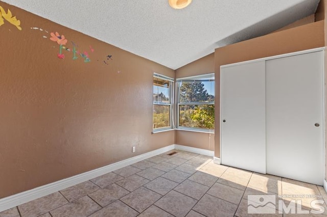 unfurnished bedroom with a textured ceiling, vaulted ceiling, light tile patterned floors, and a closet