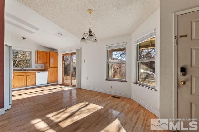 unfurnished dining area with sink, an inviting chandelier, a textured ceiling, lofted ceiling, and light hardwood / wood-style flooring