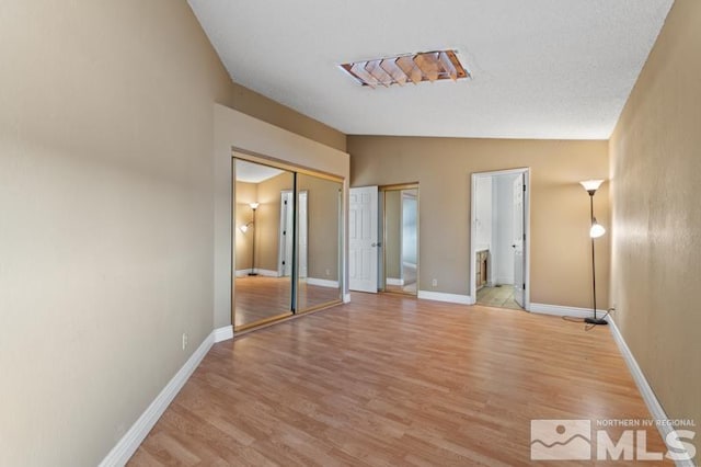 unfurnished bedroom with ensuite bath, light hardwood / wood-style flooring, a closet, and lofted ceiling