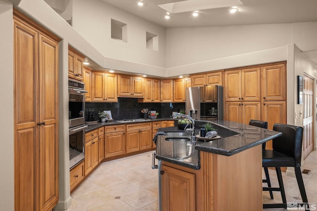 kitchen featuring a kitchen breakfast bar, stainless steel appliances, an island with sink, high vaulted ceiling, and sink