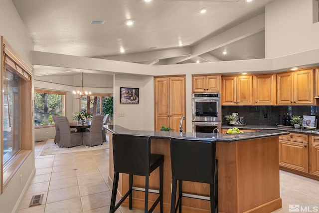 kitchen with an island with sink, a notable chandelier, light tile patterned floors, tasteful backsplash, and double oven