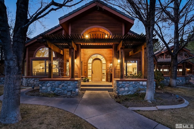 view of exterior entry featuring covered porch and a pergola