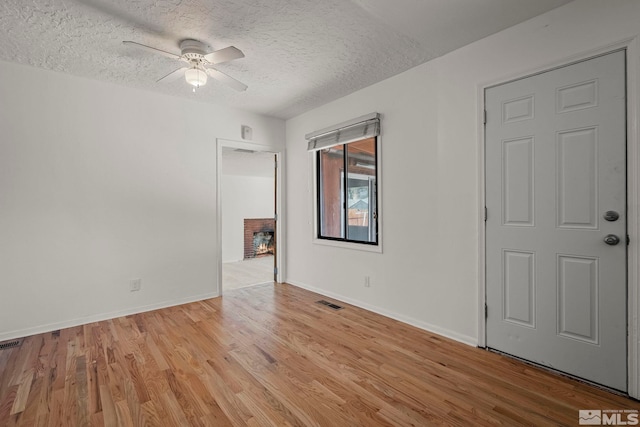 unfurnished room with a fireplace, a textured ceiling, ceiling fan, and light wood-type flooring