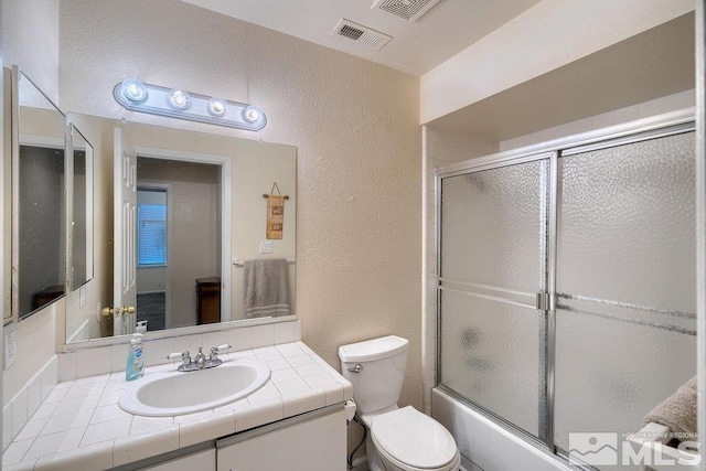 full bathroom featuring combined bath / shower with glass door, vanity, and toilet