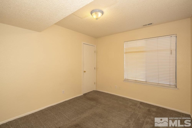 spare room with a textured ceiling and dark carpet