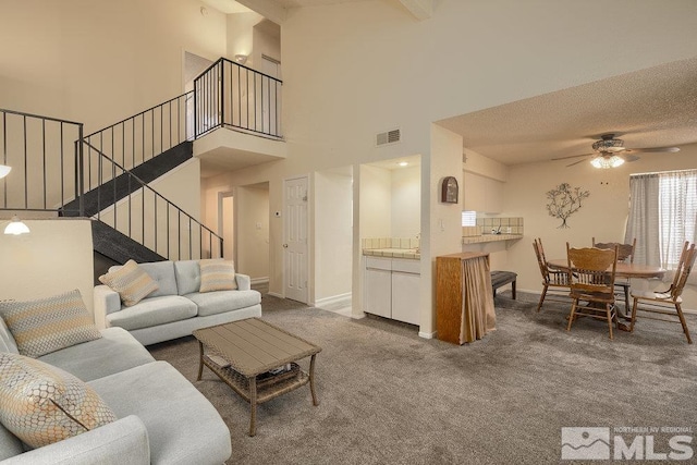 carpeted living room with ceiling fan, a towering ceiling, and a textured ceiling