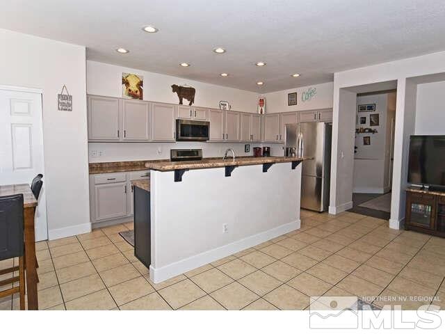 kitchen featuring appliances with stainless steel finishes, a breakfast bar area, gray cabinets, and a center island with sink