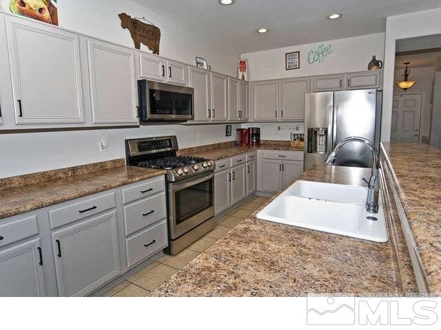 kitchen featuring appliances with stainless steel finishes, gray cabinetry, light tile patterned floors, light stone counters, and sink