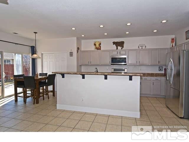 kitchen with a kitchen bar, hanging light fixtures, a kitchen island with sink, gray cabinetry, and appliances with stainless steel finishes