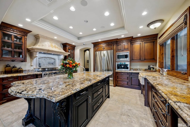 kitchen with built in appliances, a large island, light stone countertops, and custom exhaust hood