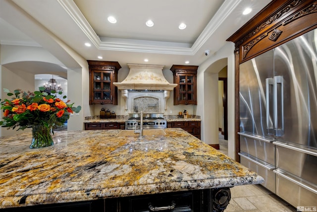 kitchen with high quality appliances, premium range hood, a tray ceiling, and light stone counters