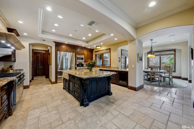 kitchen featuring stainless steel appliances, light stone counters, a center island with sink, crown molding, and wine cooler