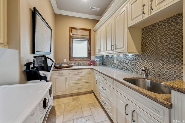 kitchen with washing machine and clothes dryer, ornamental molding, light stone counters, sink, and tasteful backsplash