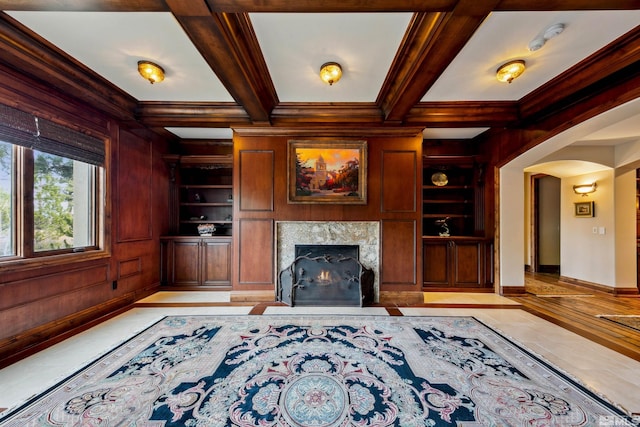 unfurnished living room featuring coffered ceiling, a premium fireplace, wood walls, built in shelves, and beamed ceiling